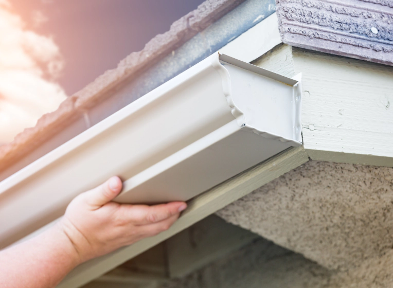 worker installing some white seamless gutters on a house